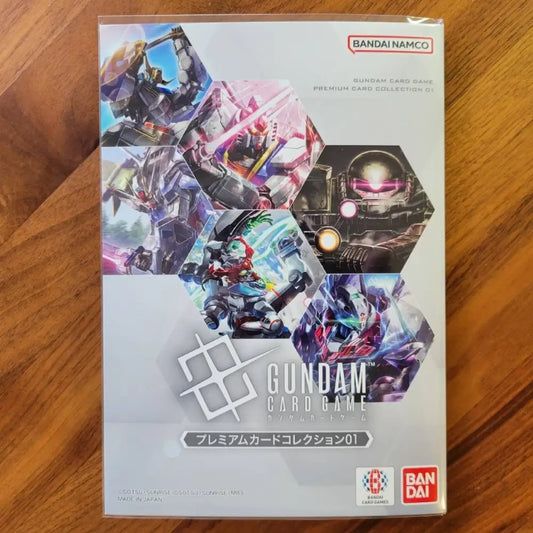 Bandai Namco Gundam Card Game Premium Card Collection 01 card box on a wooden surface, featuring colorful mecha illustrations on the front.