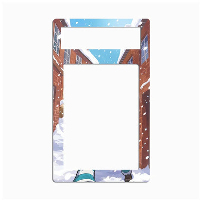 A rectangular picture frame with rounded corners, featuring an anime-style winter scene printed on the border. The illustration shows snow-covered brick buildings, falling snow, a blue sky, and a small character at the bottom.