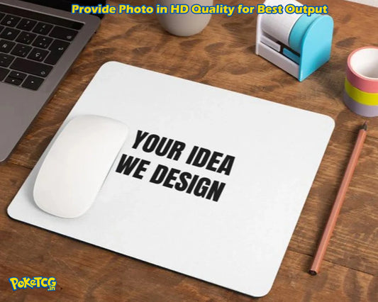 A white rectangular desk mat with rounded corners on a wooden desk, printed with the black text 'YOUR IDEA WE DESIGN'. A white computer mouse rests on the left side of the mat.