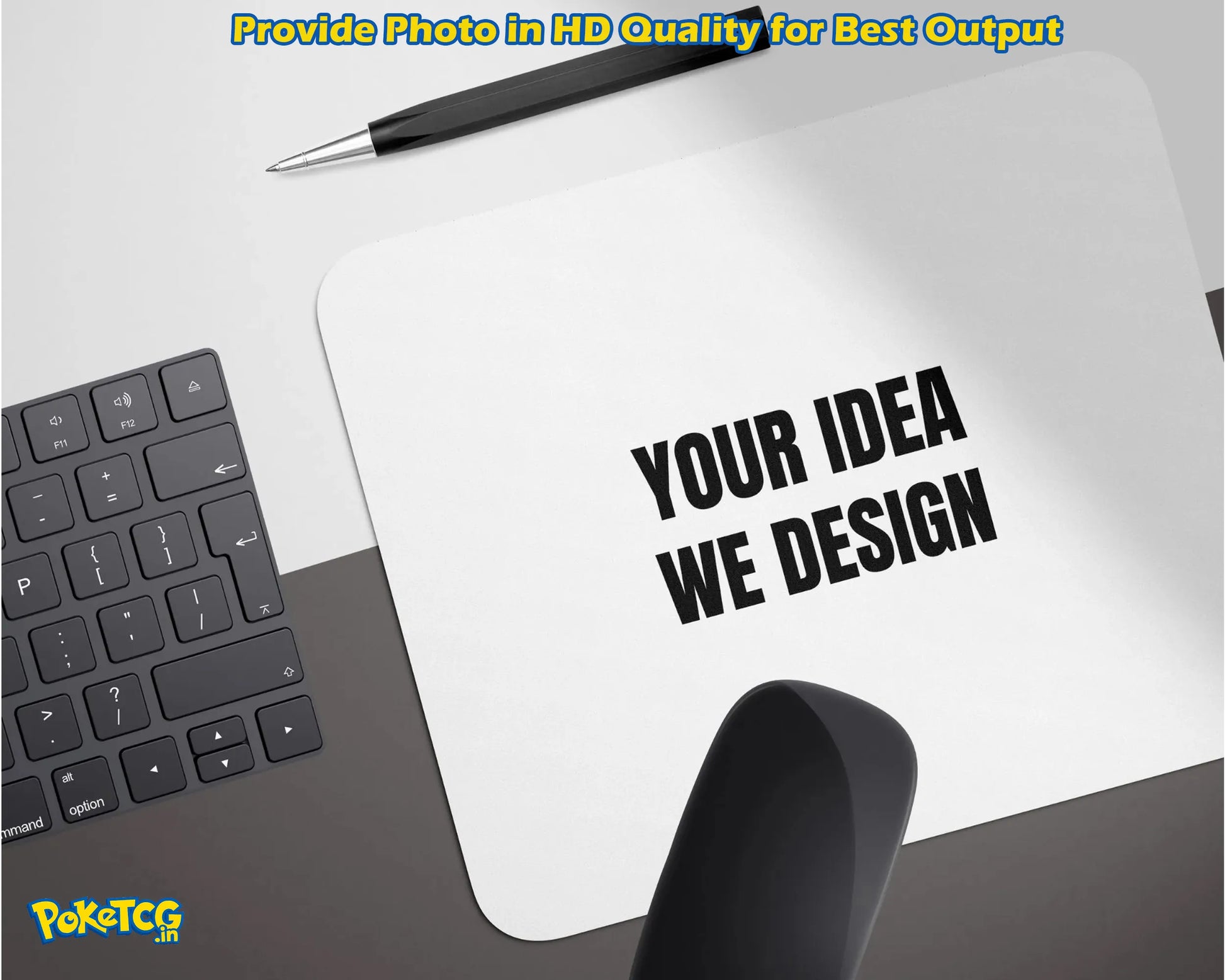 A white rectangular mockup pad or sign on a desk with the text 'YOUR IDEA WE DESIGN' in bold black letters. A black pen rests above it, with part of a keyboard on the left and a black object in the foreground.