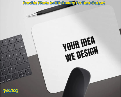 A white rectangular mockup pad or sign on a desk with the text 'YOUR IDEA WE DESIGN' in bold black letters. A black pen rests above it, with part of a keyboard on the left and a black object in the foreground.