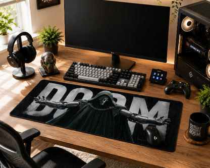 A large black gaming desk mat featuring a graphic of a hooded figure with outstretched arms and the word 'DOOM' in bold white letters, styled on a wooden desk with a keyboard, monitor, headphones, and other desk accessories.