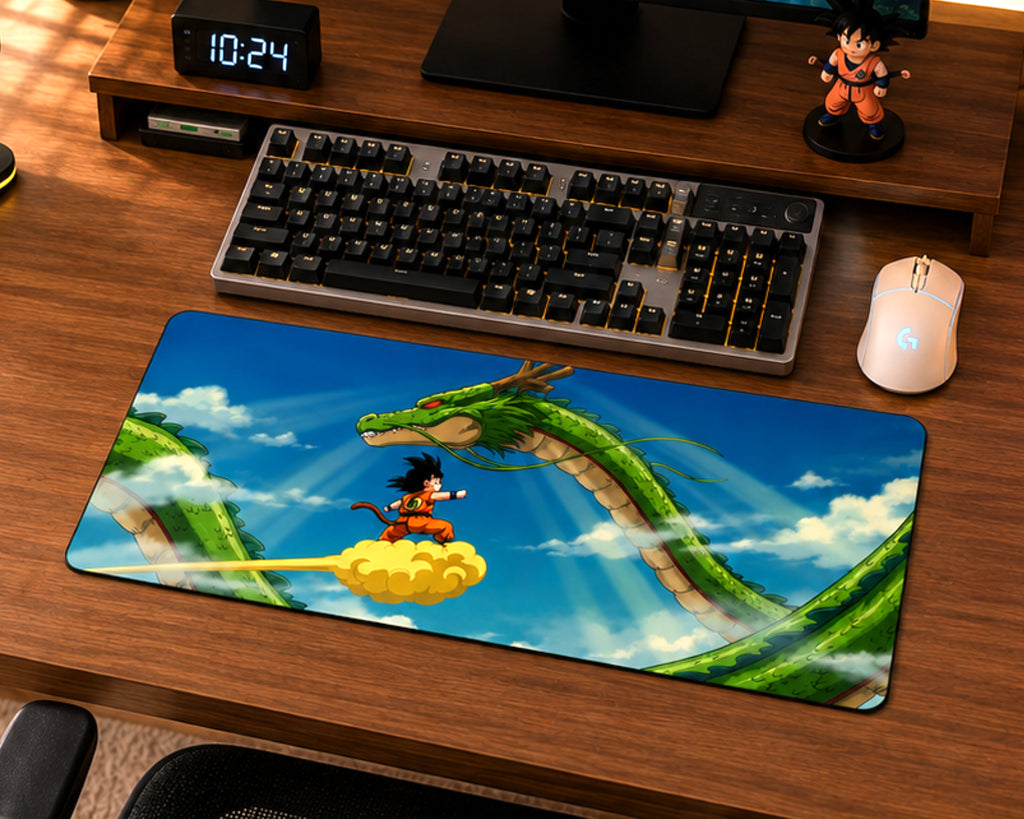 A large desk mat featuring an anime Dragon Ball scene with Goku riding a yellow cloud alongside the green Dragon, displayed on a wooden desk next to a keyboard, mouse, and other desk accessories.