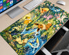 A large desk mat featuring a colorful illustration of various Pokémon Eeveo family members in a lush forest stream scene, shown on a light wood desk next to a keyboard, mouse, and computer monitor.