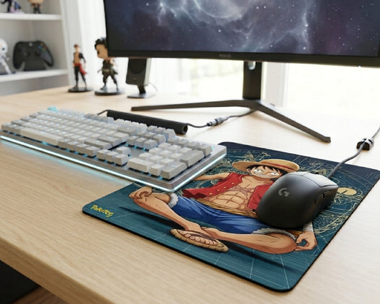 One Piece Luffy anime gaming mouse pad with seated character artwork beside white mechanical keyboard and gaming monitor setup