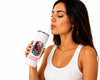 A woman with dark hair wearing a white ribbed tank top is shown from the side, drinking from a white insulated tumbler with a clear straw. The tumbler features a colorful graphic of Spider-Man and the red Marvel logo near the bottom.