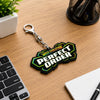A Mega Evolution Perfect Order keychain with a silver clasp, resting on a wooden desk next to a keyboard, notebook, and plant.