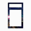 A decorative phone case or frame insert with a large blank white center and a smaller blank white top section, bordered by a dark night-sky and cityscape print with stars, colorful nebulae, and glowing windows.