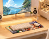 A large desk mat with a colorful anime-style print is placed on a light wood desk, supporting a white keyboard and white mouse. A computer monitor, speakers, and desk accessories are visible in the background.