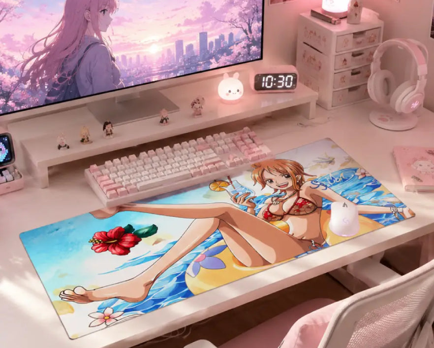 A large anime desk mat featuring Nami from One Piece in a swimwear scene, styled on a white desk in a pink-themed room with a keyboard, monitor, and headphones.