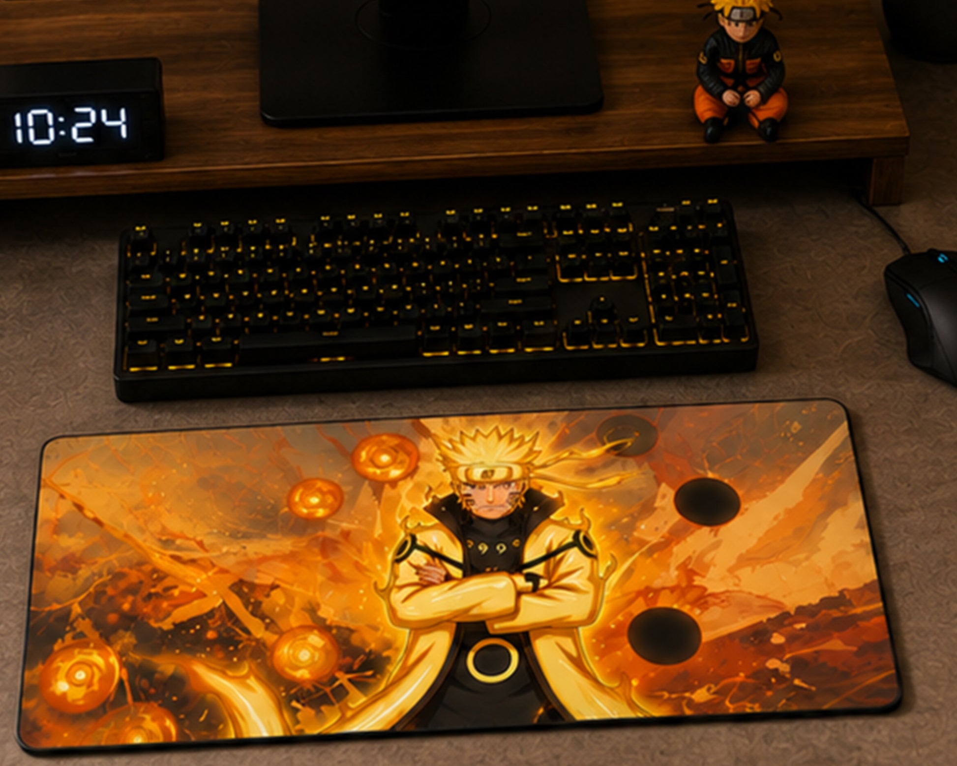 A large rectangular gaming mousepad featuring an anime character with crossed arms in a black and orange outfit against a fiery orange background, styled on a desk with a keyboard, mouse, and a small figurine.