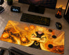 A large gaming desk mat featuring an anime character with crossed arms surrounded by glowing orange energy effects, displayed on a gray desk alongside a keyboard, mouse, monitor, and small figurine.