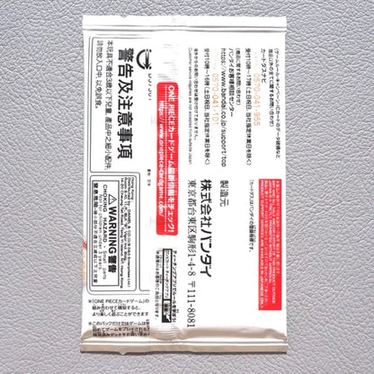 A single white rectangular product packet with dense black Japanese text and red warning panels, photographed flat against a light gray textured background.