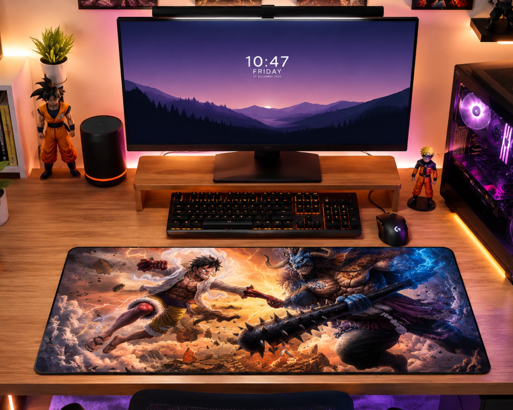 A large rectangular desk mat with a detailed anime battle illustration is laid out on a wooden desk in a styled home office setup. The desk setup includes a large monitor, keyboard, mouse, and various decorative figurines, with warm ambient lighting and a glowing PC case in the background.