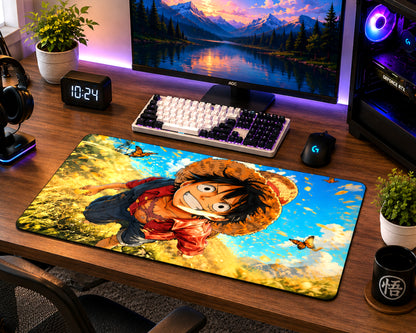 A large desk mat featuring an anime character print from One Piece, displayed on a wooden gaming desk alongside a keyboard, mouse, monitor, and plants.