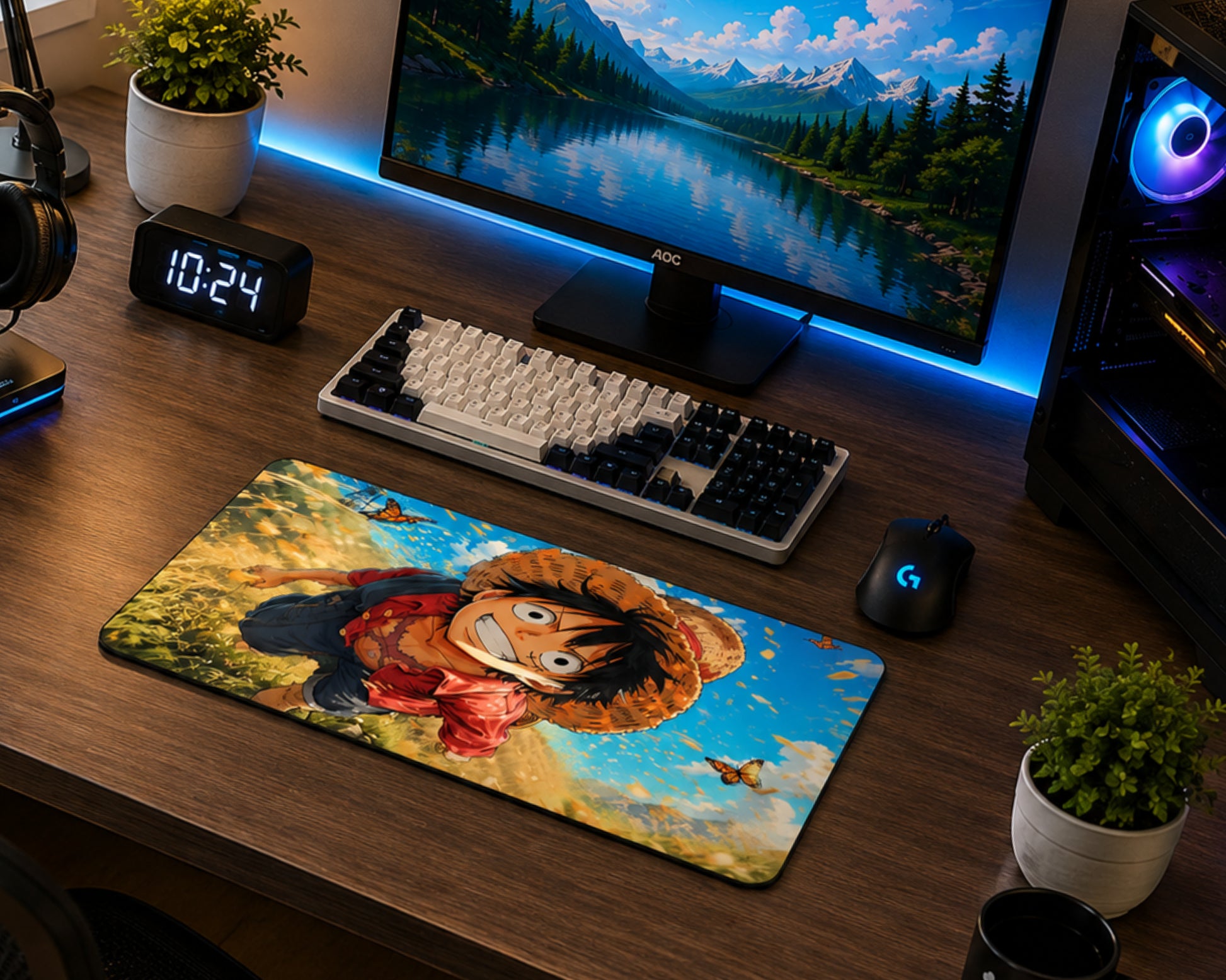 A large desk mat featuring a colorful anime-style character illustration is placed on a wooden desk in a gaming setup, alongside a keyboard, mouse, monitor, and small plants.