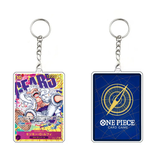 Two One Piece Card Game acrylic keychains shown side by side on a plain white background. The left keychain features a colorful character illustration with the text 'AFARO' and '12000 JT', while the right keychain has a dark blue background with a gold compass design and the text 'ONE PIECE CARD GAME'.