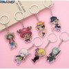 A set of seven anime keychains featuring characters from One Piece, arranged on a pink background with a beige book in the corner. The keychains are made of translucent acrylic with silver metal key rings and chains.