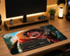 A large desk mat featuring an anime character print, styled on a wooden desk with a keyboard, mouse, monitor stand, and small plants under warm ambient lighting.