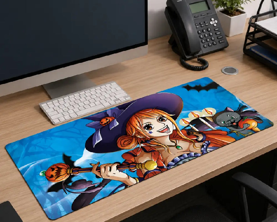 A large desk mat featuring an anime character illustration with bats and a witch hat, placed on a wooden office desk next to a keyboard, monitor, and phone.