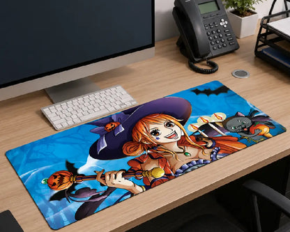 A large desk mat featuring an anime character illustration with bats and a witch hat, placed on a wooden office desk next to a keyboard, monitor, and phone.