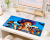 A large rectangular desk mat featuring an anime-style illustration of a witch character with orange hair, a purple hat, and Halloween-themed elements, displayed on a white desk in a styled home office setup.