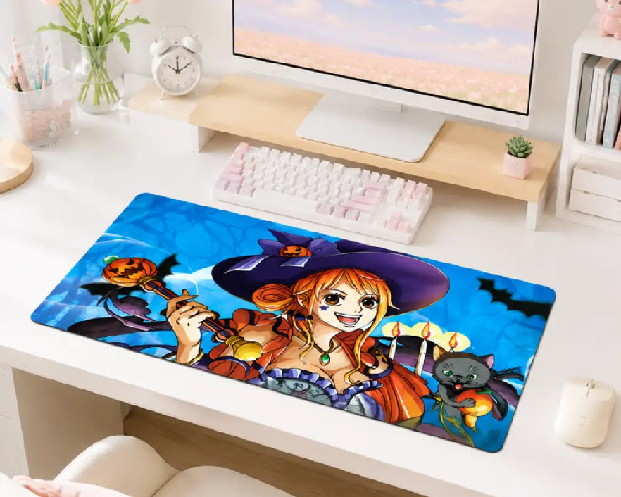 A large rectangular desk mat featuring an anime-style illustration of a witch character with orange hair, a purple hat, and Halloween-themed elements, displayed on a white desk in a styled home office setup.
