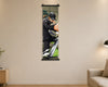 A vertical wall scroll poster hanging on a beige wall in a modern living room setting. The poster features a printed graphic of a man in a black tracksuit and cap working on a bicycle.