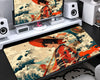 Anime-inspired extended gaming mouse pad featuring a black-haired samurai character in a red outfit holding a red umbrella, surrounded by traditional Japanese ocean waves in teal, cream, and orange, displayed on a desktop gaming setup.