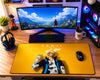 A large yellow gaming desk mat featuring an anime character print and the word 'SANJI' is laid out on a wooden desk. The setup includes a curved monitor, RGB mechanical keyboard, mouse, headphones, and a PC tower with illuminated fans.