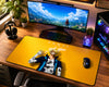 A large yellow desk mat featuring the character Sanji from One Piece, styled on a wooden desk in a gaming setup alongside a curved monitor, keyboard, mouse, headphones, and PC tower.