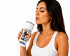 A woman with dark hair wearing a white ribbed tank top is shown from the side, drinking from a white insulated tumbler with a clear straw. The tumbler features a black and white collage graphic with a central portrait of a woman and colorful text at the bottom.