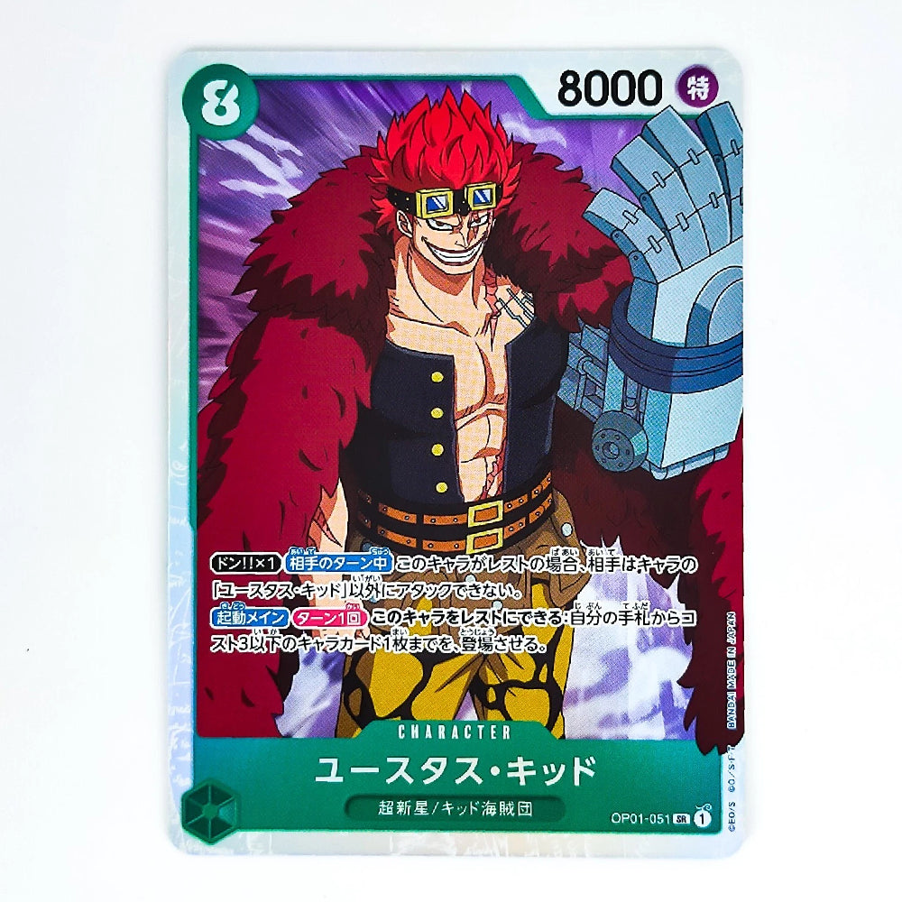 A trading card featuring the character Yustulard-Kidod from One Piece, with red hair, a large blue mechanical arm, and a dark outfit, shown on a white background.