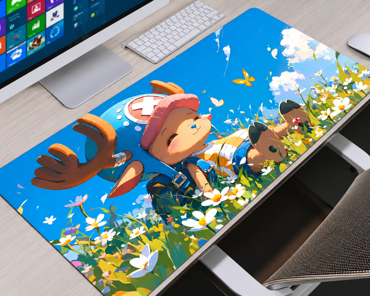 A large desk mat featuring an anime-style illustration of a character lying in a flower field under a bright blue sky, styled on a light wood desk next to a computer monitor, keyboard, and chair.