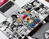 A large desk mat featuring a colorful One Piece anime character illustration over a black and white manga comic book panel background, displayed on a white desk next to a laptop.