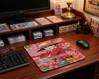 One Piece collector themed gaming desk featuring a Luffy anime mouse pad, manga volumes, trading card slabs, anime figurines, and warm wooden workstation aesthetic