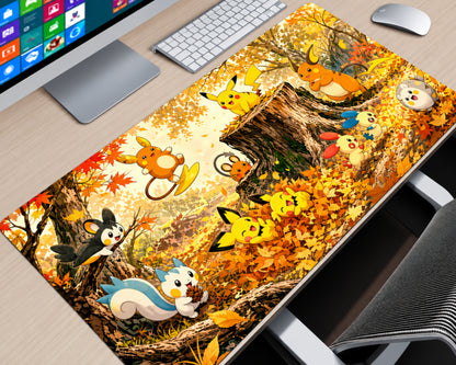 A large desk mat featuring a colorful illustration of popular Pokémon characters in an autumn forest setting, displayed on a light wood desk next to a computer monitor, keyboard, and mouse.