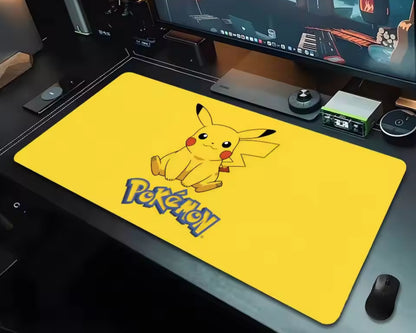 Bright yellow Pokémon extended gaming mouse pad featuring a cute Pikachu illustration with black-tipped ears, red cheeks, and the Pokémon logo, displayed on a white computer desk beneath a monitor with headphones and a keyboard nearby.