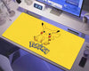 Bright yellow Pokémon extended gaming mouse pad featuring a cute Pikachu illustration with black-tipped ears, red cheeks, and the Pokémon logo, displayed on a white computer desk beneath a monitor with headphones and a keyboard nearby.