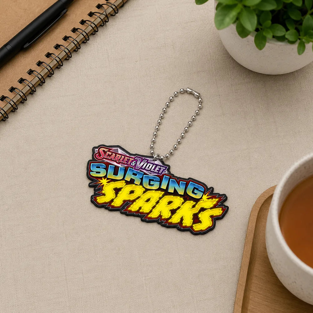 A 'Scarlet Voltage: Surging Sparks' keychain or bag charm with a silver ball chain, styled on a beige textured desk with a notebook, plant, and cup of tea.