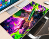 Roronoa Zoro One Piece extended gaming mouse pad featuring a green-haired swordsman holding a sword, surrounded by neon-green flames, purple and magenta smoke, glowing orange sparks, and dramatic dark textures, displayed on a light wood desk with a white keyboard, monitor, and mouse.