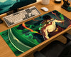 A large rectangular gaming desk mat with a colorful anime-style warrior illustration, shown on a wooden desk next to a keyboard, mouse, and monitor.