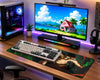 A modern gaming desk setup featuring a large curved monitor displaying a tropical beach scene, a white and black mechanical keyboard on a large illustrated mouse pad, a black computer tower with illuminated side glass, headphones on a stand, and RGB lighting under the monitor.