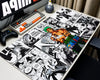 Extended One Piece anime gaming mouse pad featuring Roronoa Zoro with spiky green hair and a green waist sash, surrounded by black-and-white manga panels and a colorful One Piece logo, displayed on a white desk with a mechanical keyboard, black gaming controller, monitor, and astronaut figurine.