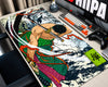 A large desk mat featuring a detailed anime-style samurai illustration, shown on a desk next to a keyboard, controller, and monitor in a home office setup.