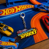 A Hot Wheels keychain featuring the 'Surging Sparks' logo, displayed on a colorful Hot Wheels toy track with toy cars.