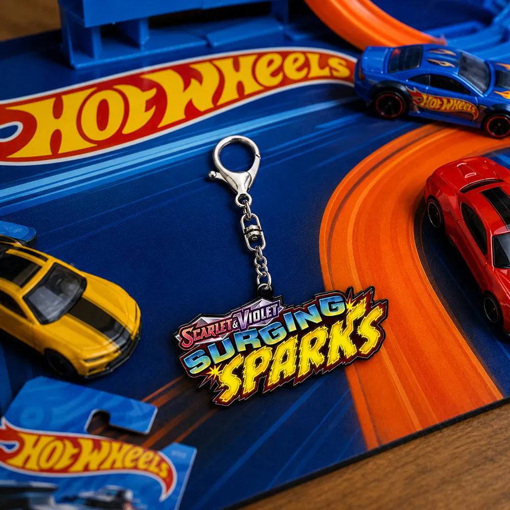 A Hot Wheels keychain featuring the 'Surging Sparks' logo, displayed on a colorful Hot Wheels toy track with toy cars.