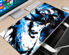 A large desk mat featuring a dynamic blue and black anime-style character design, shown on a light wood desk next to a computer monitor, keyboard, mouse, and chair.