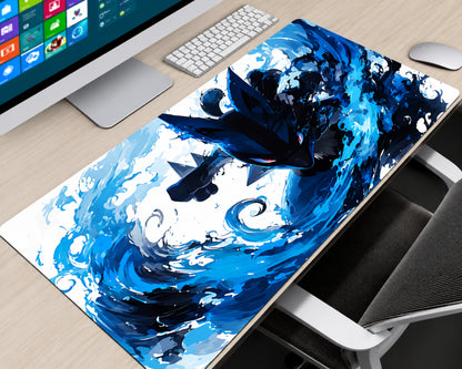 A large desk mat featuring a dynamic blue and black wave illustration with a dark bird-like creature, shown on a light wood desk next to a computer monitor, keyboard, mouse, and chair.