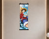 A vertical wall scroll poster featuring the anime character Monkey D. Luffy from One Piece, hanging on a beige textured wall with warm ambient lighting.